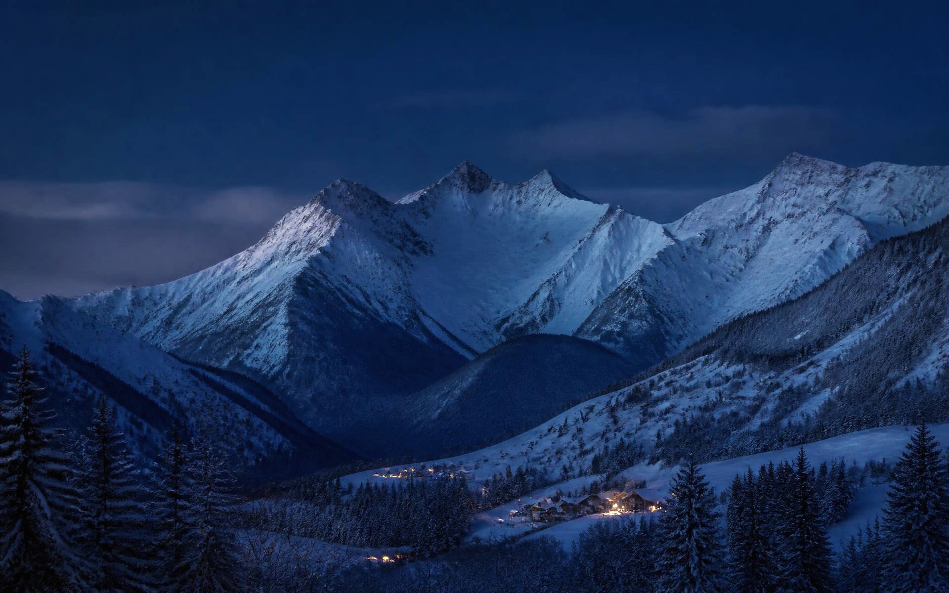 Snow-covered Alpine mountains above a winter village at blue hour